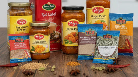 A collection of essential Indian grocery items including Priya pickles, TRS spices, and Red Label tea, representing 10 essentials for a German kitchen.