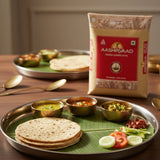Aashirvaad atta package with a plate of roti, vegetables, and chutneys on a wooden table.