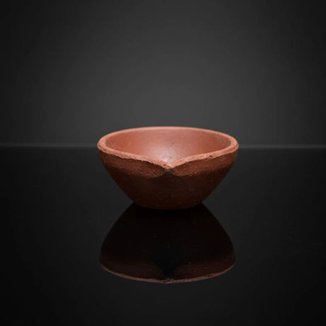 Terracotta bowl on a reflective black surface with a dark background
