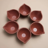 Set of six terracotta oil lamps arranged in a circle on a beige background