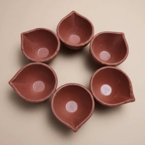 Set of six terracotta oil lamps arranged in a circle on a beige background