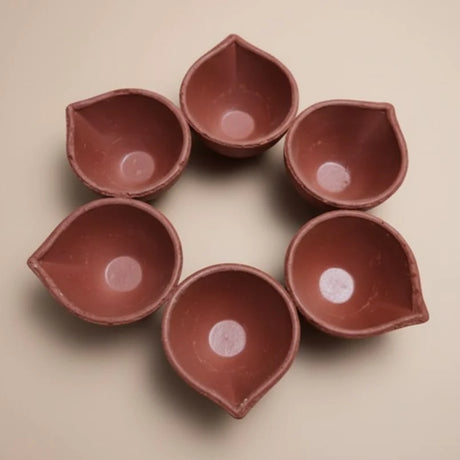 Set of six terracotta oil lamps arranged in a circle on a beige background