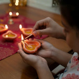 Person lighting a small clay lamp with a match during Diwali celebrations.
