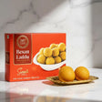 Box of Besan Laddu sweets with two laddus on a marble surface