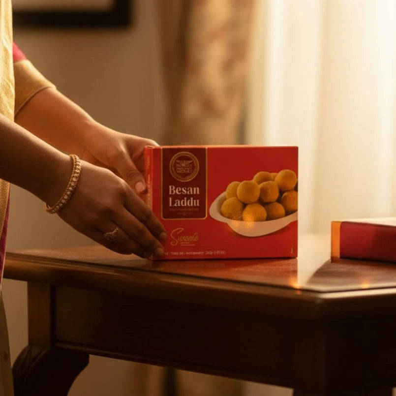 Person holding a box of Besan Laddu on a wooden table with a blurred background