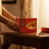 Person holding a box of Besan Laddu on a wooden table with a blurred background