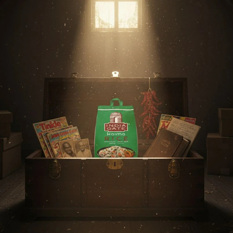 Open suitcase with vintage items including a bag of India Gate rice, comic books, and a passport in a dimly lit room.