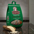 Green bag of India Gate Kaima Rice with a scoop of rice on a dark surface