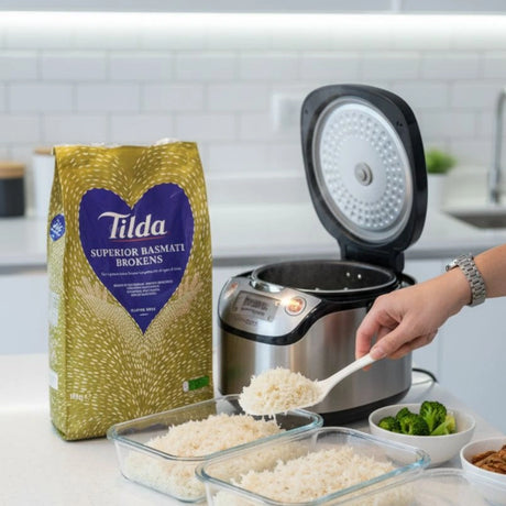 Person scooping rice from a Tilda bag into containers on a kitchen counter.